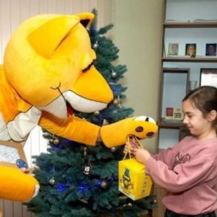 Mascot giving a gift to a child by a Christmas tree