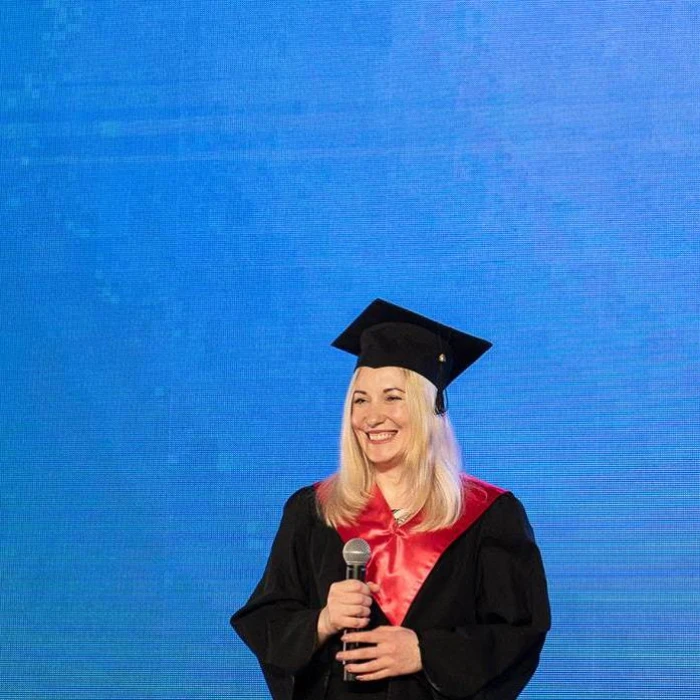 Woman in graduation cap and gown speaking on stage