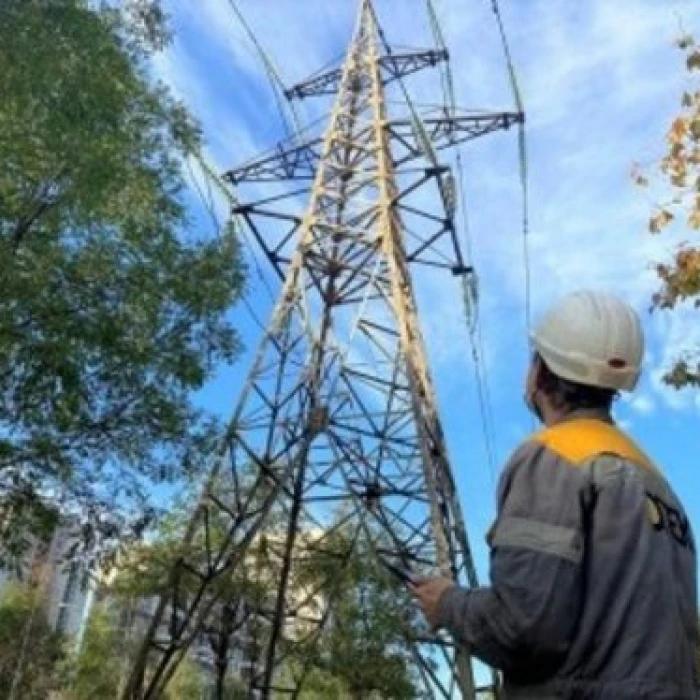 Electrical worker standing near a steel transmission pylon with overhead power lines